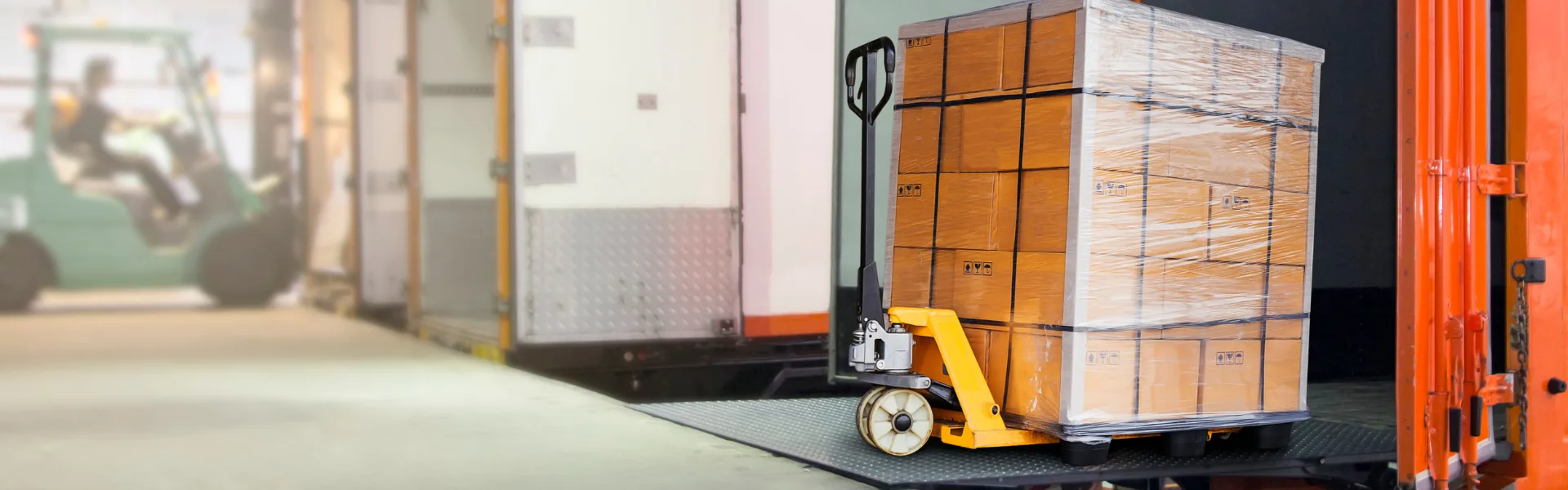 Pallet wrapped with cartons being loaded into a freight truck using a pallet jack, representing logistics and freight handling.